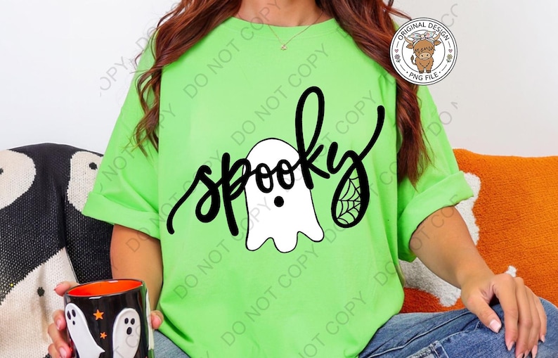 Op de afbeelding: Een fel limoengroen t-shirt met een zwart grafisch ontwerp met het woord spooky in cursief schrift. Het ontwerp bevat een witte geestillustratie met een zwarte stip als oog en een klein spinnenwebdetail op de letter y.