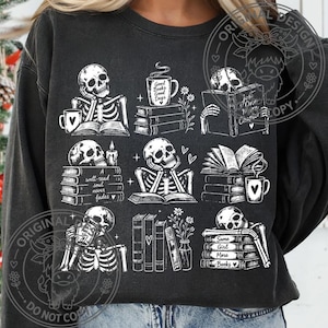 May include: A charcoal gray crewneck sweatshirt featuring a white graphic print of nine distinct scenes with skeletons reading books, drinking from mugs, and flowers. The text includes phrases like Good Books Good Days and A well-read soul never fades.