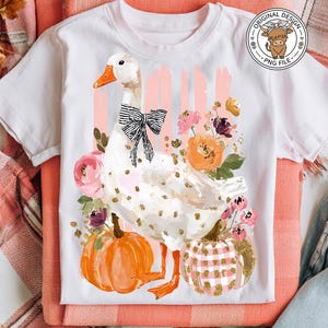 May include: White t-shirt featuring a goose illustration with a black bow, surrounded by flowers and pumpkins. The design includes gold polka dots and the text "Original Design PNG File".