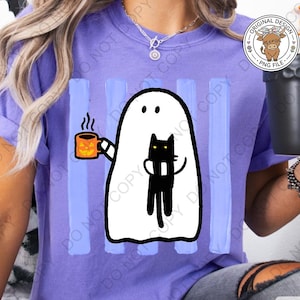 May include: A light purple t-shirt featuring a graphic of a white ghost holding an orange jack-o'-lantern mug with steam rising and a black cat. The design is set against vertical light blue stripes. The shirt has short sleeves and a crew neckline.