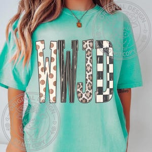 May include: A turquoise short-sleeve t-shirt featuring the letters WWJD printed across the chest. Each letter has a distinct pattern: the first W has brown polka dots, the second W has black vertical stripes, the J has a leopard print, and the D has a black and white checkerboard pattern.
