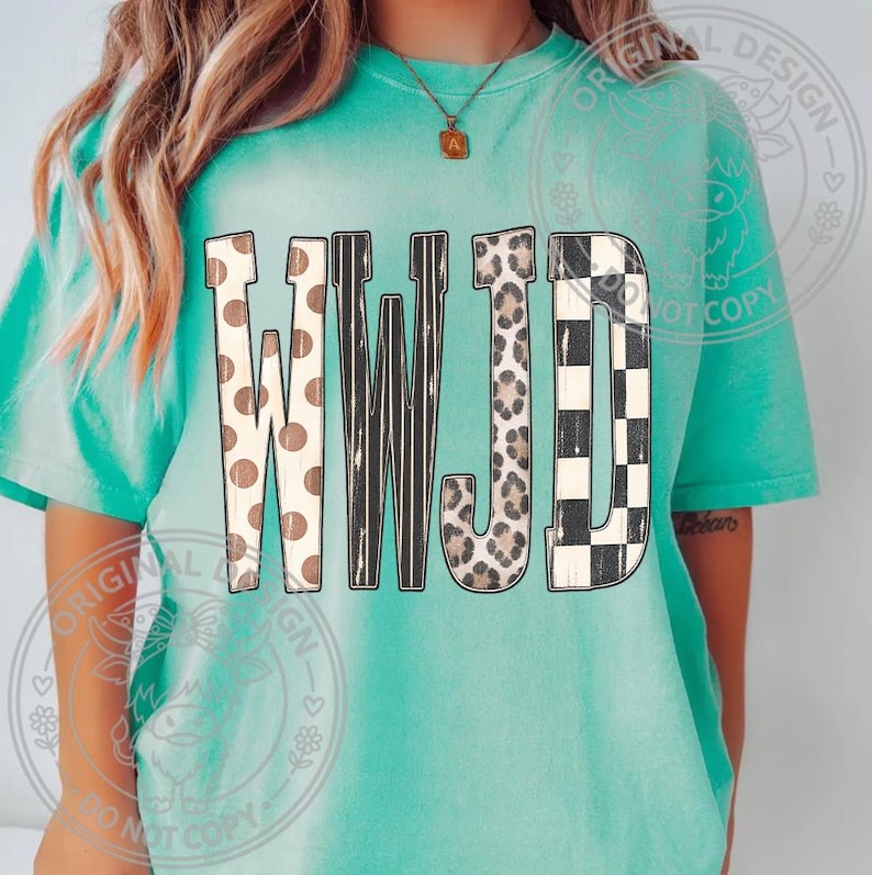 May include: A turquoise short-sleeve t-shirt featuring the letters WWJD printed across the chest. Each letter has a distinct pattern: the first W has brown polka dots, the second W has black vertical stripes, the J has a leopard print, and the D has a black and white checkerboard pattern.