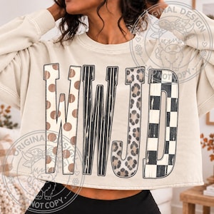 May include: A beige long-sleeve sweatshirt featuring the letters WWJD in a large graphic print. Each letter has a distinct pattern: the Ws feature brown polka dots and black vertical stripes, the J has a leopard print, and the D has a black checkerboard.