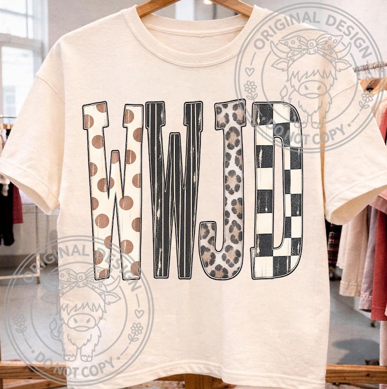 May include: A cream-colored short-sleeve t-shirt featuring the letters WWJD in a large, bold font. Each letter has a distinct pattern: the Ws feature brown polka dots and black vertical stripes, the J has a leopard print, and the D has a black and white checkerboard pattern.