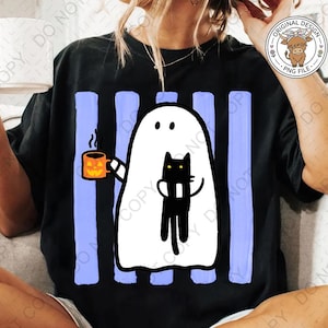 May include: A black t-shirt featuring a graphic of a white ghost holding an orange jack-o'-lantern mug and carrying a black cat. The design is set against a background of vertical light blue stripes. The shirt has a round neckline and short sleeves.