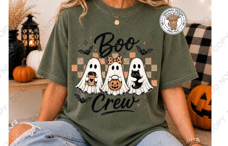 May include: An olive green t-shirt featuring a graphic of three white ghosts with the text "Boo Crew". The center ghost wears a polka dot bow, while the others hold a coffee cup, a jack-o'-lantern bucket, and a black cat. Bats and stars surround them.