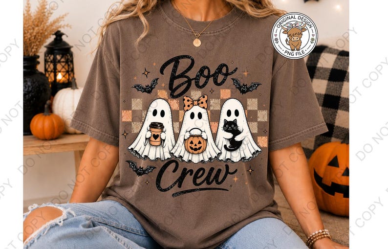 May include: A brown short-sleeve t-shirt featuring a graphic of three white ghosts with the text "Boo Crew". The ghosts are holding a coffee cup, a pumpkin bucket, and a black cat. The design includes bats and a checkered background.