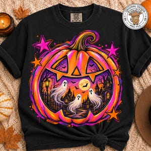May include: A black short-sleeve t-shirt featuring a large, vibrant orange jack-o'-lantern graphic. Inside the pumpkin are three white ghosts, a haunted house, a full moon, and bats. The design is accented with bright pink and orange stars.