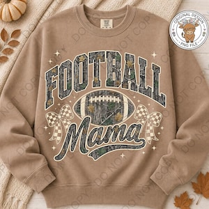 May include: A tan crewneck sweatshirt featuring a graphic print with the text FOOTBALL MAMA in a camouflage pattern. The design includes a football, two checkered bows, and small star accents. The sweatshirt has long sleeves and a ribbed neckline.