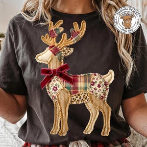 Può includere: Una t-shirt grigio scuro con una grafica centrale di una renna composta da vari ritagli di tessuto, inclusi motivi a quadri, floreali, leopardati e a righe. La renna ha un fiocco in velluto rosso scuro al collo e un logo circolare nell'angolo.