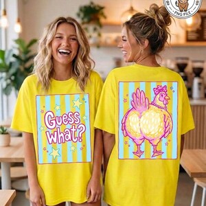 May include: Two yellow t-shirts with matching designs. The front of the shirt says "Guess What?" in a playful font with stars. The back of the shirt features a cartoon chicken with a pink crown and necklace.