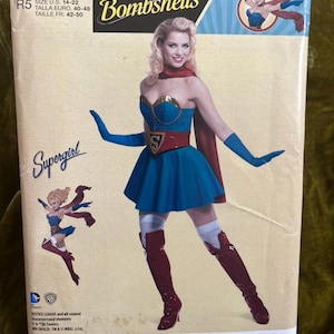 May include: A Simplicity sewing pattern featuring a DC Comics Bombshells Supergirl costume. The pattern includes a blue dress, red cape, and boots. The size range is U.S. 14-22. The package has the Supergirl logo and illustrations.