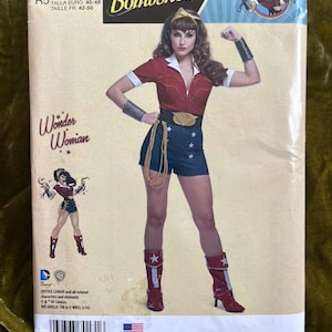 May include: A Simplicity sewing pattern for a DC Comics Bombshells Wonder Woman costume. The pattern features a full-body image of the costume, which includes a red top, blue shorts, and red boots. The pattern size is US 14-22.