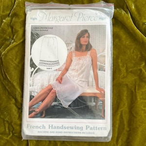 Könnte beinhalten: Ein Vintage-Schnittmuster von Margaret Pierce für einen Damen-Unterrock. Die Verpackung zeigt eine Zeichnung des Unterrocks und eine Frau, die ein passendes Oberteil und einen Rock trägt. Der Text "French Handsewing Pattern" ist sichtbar.