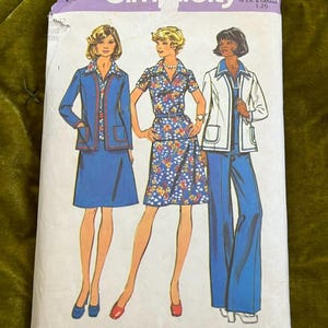 May include: Vintage Simplicity sewing pattern featuring three women modeling different outfits. The outfits include a blue skirt suit, a floral print dress, and a white jacket with blue pants. The pattern is labeled "Look Slimmer pattern".