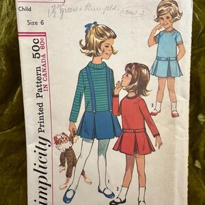 Könnte beinhalten: Vintage Simplicity Schnittmuster für Kindergröße 6. Das Muster zeigt Illustrationen von Mädchen in Kleidern mit Hosenträgern und Faltenröcken. Der Text "50c" und "IN CANADA 60c" ist auf dem Muster zu sehen.