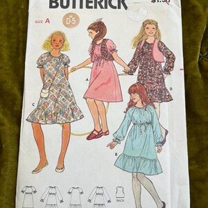 Può includere: Modello di cucito Butterick vintage 6256 per abiti da ragazza. La copertina del modello presenta illustrazioni di quattro diversi stili di abito, con un prezzo di $1,50. Il design include una varietà di lunghezze di abito e stili di maniche.