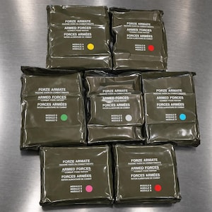 May include: A collection of olive green military combat food ration packs. Each pack is labelled with text in multiple languages, including "Armed Forces" and "Combat Food Ration." Various coloured dots, like yellow, red, and green, are visible.