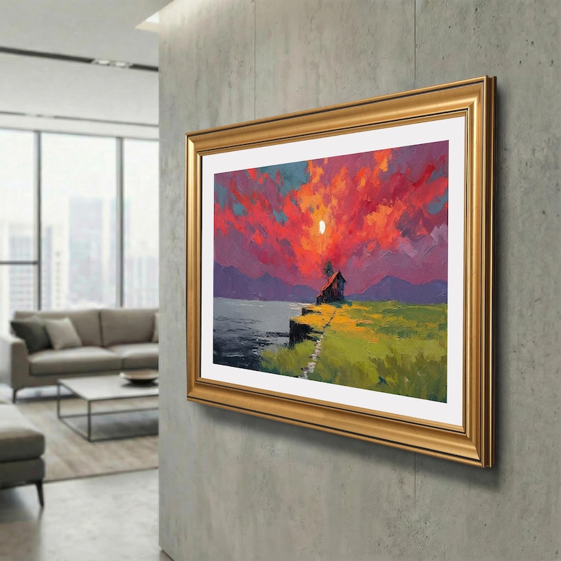 May include: A framed landscape painting shows a small house on a cliff overlooking a lake, under a vibrant sunset. The sky is a mix of red, orange, and purple hues, with a bright sun. The frame is gold.