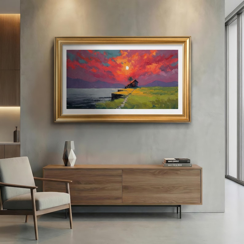 May include: A framed landscape painting shows a sunset over water. The sky is a mix of red and orange, with a small house on the horizon. The painting is in a gold frame, and is a piece of wall art.