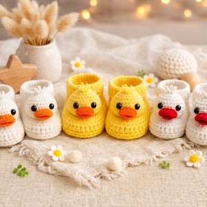 May include: Crocheted baby booties in white and yellow, shaped like ducks. The white booties have red beaks, while the yellow ones have orange beaks. The booties are arranged on a neutral-colored fabric, with decorative flowers and a vase in the background.