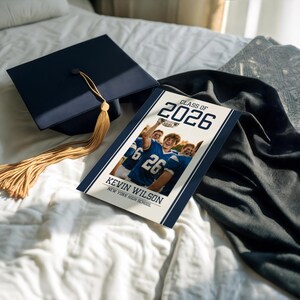 May include: A navy blue graduation cap with a gold tassel rests near a graduation announcement. The announcement features a photo of students in blue jerseys, the text "Class of 2026," and the name "Kevin Wilson."
