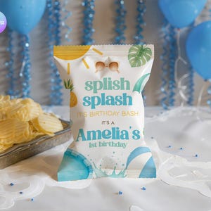 Può includere: Un sacchetto di patatine bianco con la scritta "splish splash" e "It's Amelia's 1st birthday". La borsa ha un tema spiaggia con occhiali da sole, ananas e foglia di palma. Palloncini blu e patatine sullo sfondo.