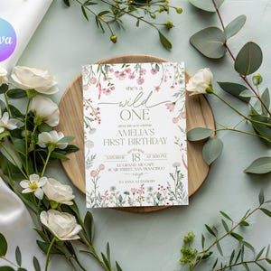 Puede incluir: Una invitaci&oacute;n de cumplea&ntilde;os con detalles florales y el texto "she's a wild ONE". La invitaci&oacute;n est&aacute; sobre un plato de madera, rodeada de rosas blancas y vegetaci&oacute;n. La invitaci&oacute;n incluye el nombre "Amelia" y detalles del evento.