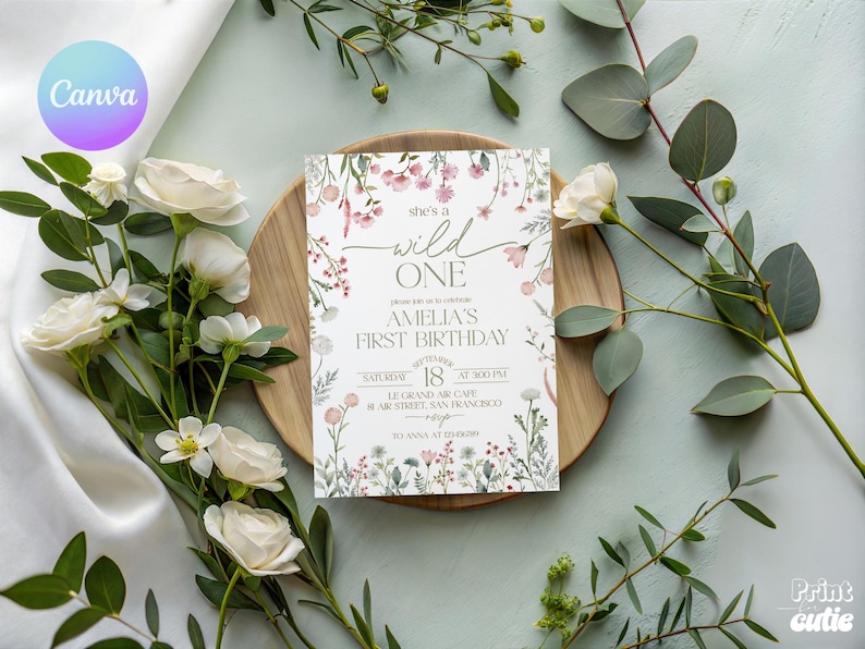 Puede incluir: Una invitaci&oacute;n de cumplea&ntilde;os con detalles florales y el texto "she's a wild ONE". La invitaci&oacute;n est&aacute; sobre un plato de madera, rodeada de rosas blancas y vegetaci&oacute;n. La invitaci&oacute;n incluye el nombre "Amelia" y detalles del evento.