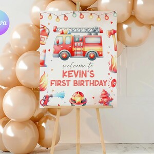 May include: A birthday sign for Kevin, with a red fire engine, fire-related illustrations, and the text "Welcome to Kevin's First Birthday." The sign is on a wooden easel, with a balloon arch in the background. The sign is in cm.