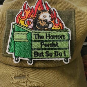 May include: A white ceramic mug with a black handle and the text "But First, Coffee" in a bold, black font. The mug is set against a blurred background, suggesting a cozy setting.