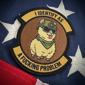May include: Embroidered patch featuring a cartoon llama wearing a military helmet and sunglasses. The patch has the text "I IDENTIFY AS" above the llama and "A FUCKING PROBLEM" below. The patch is on a blue background with white stars and red stripes.