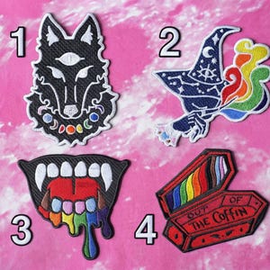 May include: Four embroidered patches with unique designs. A black wolf with a third eye, a blue witch hat with a rainbow plume, a mouth with rainbow drool, and a red coffin with the text "OUT OF THE COFFIN" and a rainbow inside.