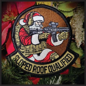 May include: Embroidered patch featuring Santa Claus in tactical gear, holding a rifle. The patch is circular with a brown background and a black border. Text on the patch reads "SLOPED ROOF QUALIFIED" in gold lettering.