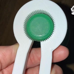 Può includere: Un apribottiglie bianco con un design circolare, con un tappo verde. L'apribottiglie ha un meccanismo a ingranaggi per afferrare e ruotare i tappi delle bottiglie. Il design è stampato in 3D.