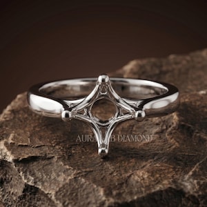 May include: A polished silver-toned metal ring setting featuring a four-prong head designed to hold a single gemstone. The band is smooth and rounded, and the text AURA LAB DIAMOND is visible on the metal structure of the ring setting.