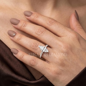 May include: A marquise-cut diamond engagement ring with a pavé band. The ring is set on a hand with a neutral manicure. The text "AURA LAB DIAMOND" is visible.