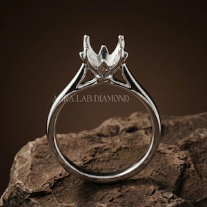 May include: A polished silver-toned metal ring setting featuring a six-prong head designed to hold a single gemstone. The band is smooth and circular, with the text AURA LAB DIAMOND clearly visible across the center of the ring's opening.