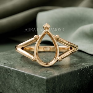 May include: A rose gold ring setting featuring a pear-shaped center mount with four small prongs and a geometric, open-frame design. The metal has a polished finish, and the text AURA LAB DIAMOND is visible in the background behind the ring.