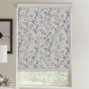 Könnte beinhalten: Ein weißer Rollvorhang mit einem sich wiederholenden Muster aus blauen und grauen Zweigen und Blättern. Der Vorhang ist teilweise heruntergelassen und bedeckt den oberen Teil eines Fensters. Das Fenster zeigt eine Aussicht auf Bäume und Grün draußen.