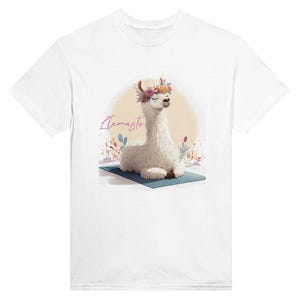 Op de afbeelding: Wit t-shirt met een aquarel illustratie van een lama met een bloemenkrans, zittend op een blauwe yogamat. Het woord "Llamaste" is cursief geschreven. De lama staat tegen een zachte gele achtergrond met bloemaccenten.