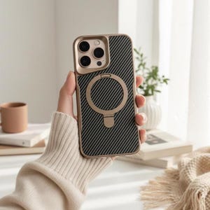 May include: A gold and black phone case with a carbon fiber pattern. The case has a gold ring and a camera cutout. The phone case is designed to fit a smartphone. The case is held in a person's hand.