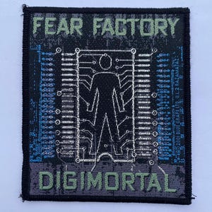 Puede incluir: Un parche tejido rectangular con borde negro. El texto superior dice FEAR FACTORY en verde claro. El centro presenta una silueta humana negra dentro de un marco de placa de circuito blanco. El texto inferior dice DIGIMORTAL en verde claro.