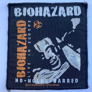 May include: A square black embroidered patch featuring the white text BIOHAZARD at the top and NO HOLDS BARRED at the bottom. It includes the orange text BIOHAZARD LIVE IN EUROPE, a biohazard symbol, and a stylized white graphic of a person's face.