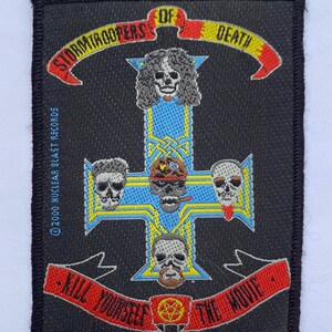 May include: A rectangular black embroidered patch featuring a blue cross with yellow borders. The design includes five skulls, a red banner with the text Stormtroopers of Death, and a red banner with the text Kill Yourself The Movie.