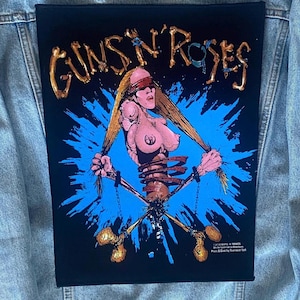 May include: Black patch with the Guns N' Roses logo in gold. The graphic shows a skeleton woman with long blonde hair, holding her hair, set against a blue burst background with crossed bones.