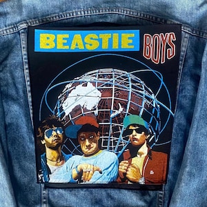 May include: Light blue denim jacket with a large patch featuring the words "BEASTIE BOYS" in yellow and red. The patch includes an illustration of the band members and a globe graphic.