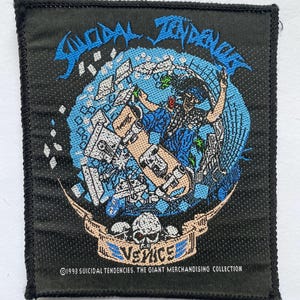 Może przedstawiać: Czarna kwadratowa naszywka z napisem "Suicidal Tendencies" w kolorze niebieskim, z grafiką skatera. Naszywka zawiera tekst "Venice" i "1993 Suicidal Tendencies. The Giant Merchandising Collection."