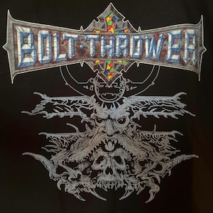 Puede incluir: Camiseta negra con el nombre de la banda "BOLT THROWER" en una fuente estilizada y multicolor. Debajo, una ilustración gris detallada de una cara demoníaca con una calavera y diseños intrincados y ramificados.