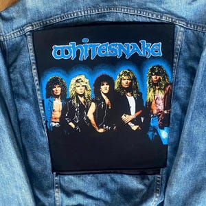 May include: A light blue denim jacket with a large black patch featuring the band Whitesnake. The patch shows a group of five men with long hair, with the band's name in blue lettering above them.